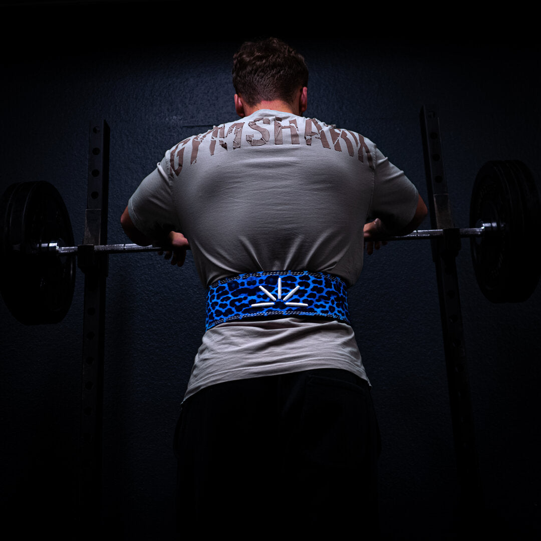 Mand med blåt Trackfie træningsbælte står foran et squat rack med hænderne på en barbell