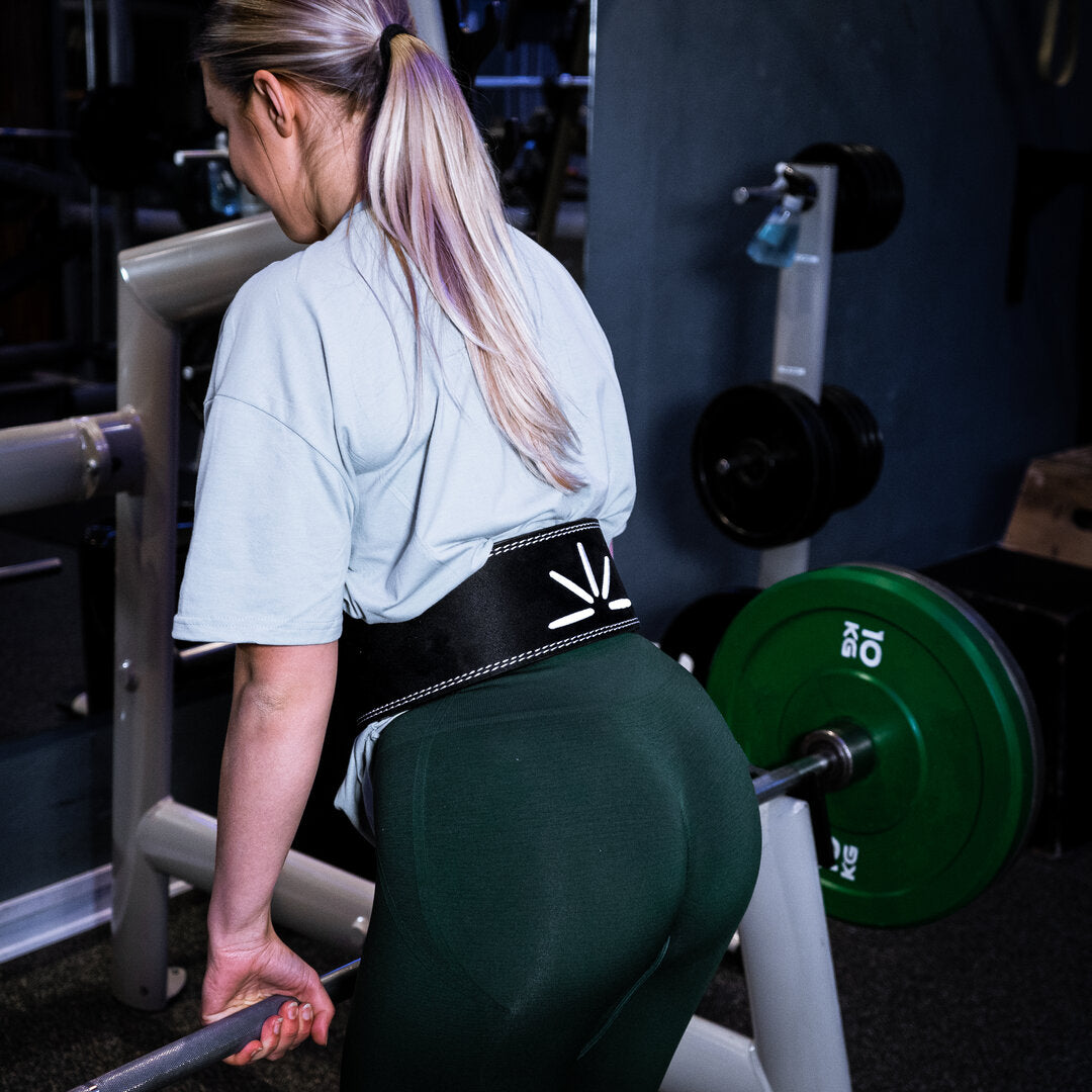 Kvinde med sort Trackfie træningsbælte laver dødløft med barbell