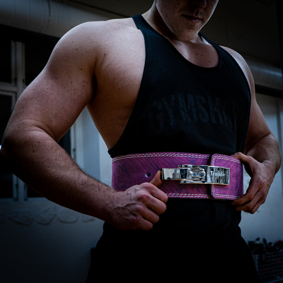 En mand iført lilla Trackfie træningsbælte står i et fitnesscenter